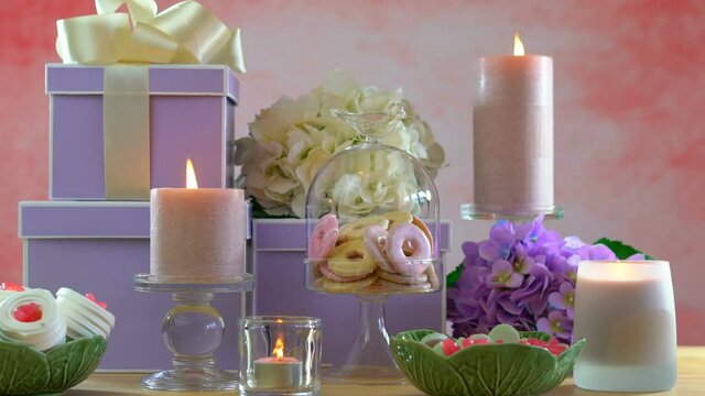 4k Mother's Day or Birthday party table with stack of gifts, cookies, flowers, and candles. Continuous loop cinemagraph with burning candles.