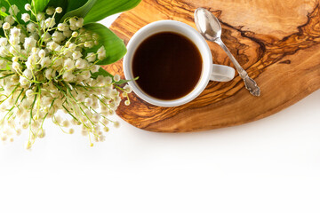 Cup of coffee and fresh bouquet of blooming lily of valley flowers on wooden stand on white background. Top view, flat lay, copy space.