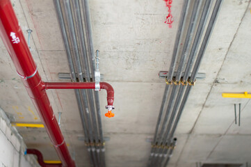 Fire sprinkler system with red pipes is placed to hanging from the ceiling inside of an unfinished new building.Installation of conduits in buildings.Conduit system in building under construction. - obrazy, fototapety, plakaty