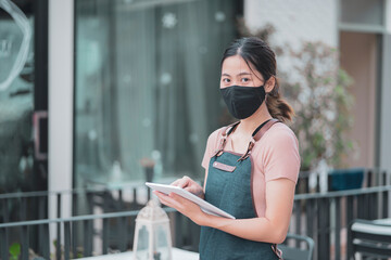 Asian barista woman worker new normal wearing facemask protection COVID-19 coronavirus pandemic using smart tablet device customer service serving food at café restaurant store small business owner