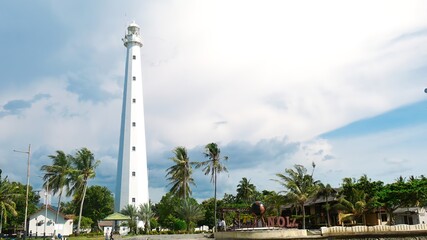 Anyer, Indonesia-March 31, 2021: a historic lighthouse building that has a white color with several windows. The sky background is blue and there are colored clouds called the Mercusuar Cikoneng