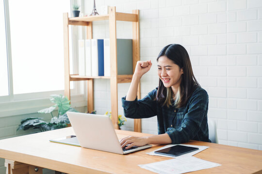 Graphic designer using graphics tablet happy Asian woman freelance worker using computer laptop technology designing innovation creative ideas plan cheering excitement success working modern office