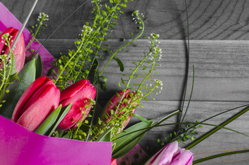 floral arrangement of pink tulips with green leaves and decor on a black and white wooden background of the kopi space