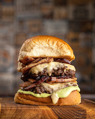 Hambúrguer duplo de carne com queijo mussarela, fatias de bacon e molho verde