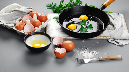 Raw eggs in pan with herbs and seasoning on gray background, prepared food for breakfast.