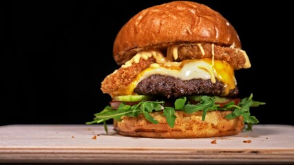 Craft burger is cooking on black background. Consist: sauce, arugula, tomato, red onion rings fries, cucumber, cheese, air bun and marble meat beef.