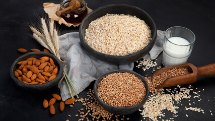 Rolled oat flakes in black bowls and golden wheat ears on dark background.
