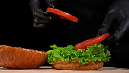 Craft burger is cooking on black background. Consist: sauce, lettuce, tomato, red onion, pickle,...