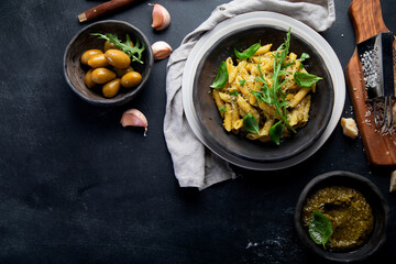 Pasta spaghetti with homemade pesto and fresh basil leaves on dark background. Italian cuisine concept.