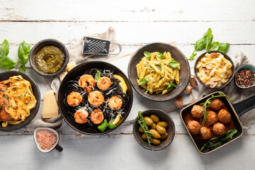 Assortment of Italian pasta with traditional snacks and sauces for dinner on white wooden background.
