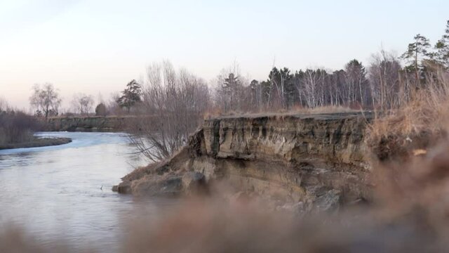 Soil erosion ditch around a running water, wild spring forest river cliff, sheer shore. Precipice and water erosion gully, vertical bank of a river panorama landscape.