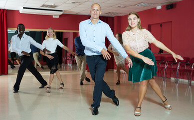 Pairs of young positive people dancing twist together at modern dance studio