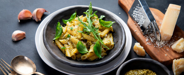 Pasta spaghetti with homemade pesto and fresh basil leaves on dark background. Italian cuisine concept.