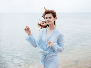 Fototapeta na wymiar A traveler in a blue dress runs along the seashore on the beach