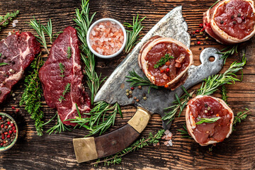 Variety of raw beef meat steaks for grilling with seasoning and herbs on old meat butcher on dark wooden background. banner, menu recipe top view