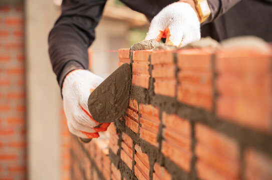 Close up hand of industrial bricklayer in glove installing bricks on construction site