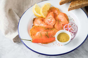 Asia Art Gravlax Graved Lachs, ein roh gebeizter Fisch mit Zitronengras und Chili auf Emaille Teller mit Hovmästarsås Senf Soße, Toast, Zwiebel Ringe, Dill, Zitrone und Leinen Tuch auf hell Marmor 