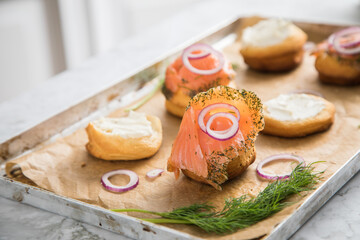 Gravlax Graved Lachs, ein roh gebeizter Fisch mit Dill auf Brötchen mit Frischkäse,  Zwiebelringe auf Backblech mit Backpapier und hell Marmor Hintergrund