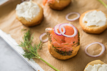 Gravlax Graved Lachs, ein roh gebeizter Fisch mit Dill auf Brötchen mit Frischkäse,  Zwiebelringe auf Backblech mit Backpapier und hell Marmor Hintergrund