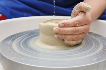 Hands making vessel daytime of white clay in fast moving circle.
