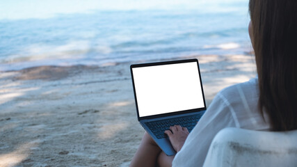 Mockup image of a woman using and typing on laptop computer with blank desktop screen while sitting on the beach