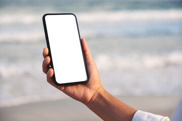 Mockup image of hands holding black mobile phone with blank desktop screen by the sea