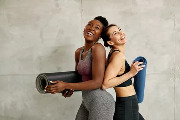 Fotobehang Young cheerful athletic women holding Yoga mats and laughing against the wall. © Drazen