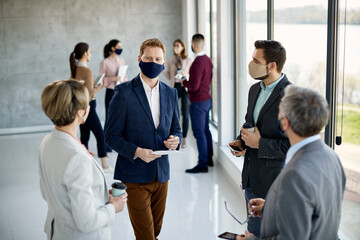Group of business people wearing face masks while talking hallway of an office building.