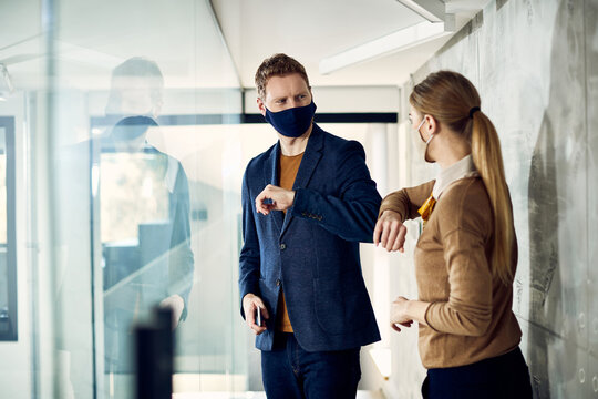 Business co-workers greeting with elbows and wearing face masks at work due to coronavirus pandemic.