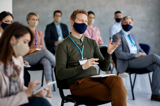 Entrepreneur with face mask talks while attending business education event in conference hall.