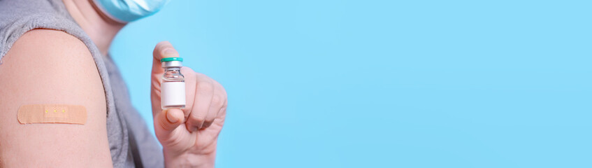 Man with a bottle of vaccine and a plaster on his shoulder after getting Covid-19 vaccine on a blue background. Medicine concept, vaccination, coronavirus immunity, safe travel. Baner. Copy space