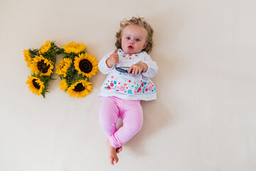 Cute little toddler girl in a white shirt lies next to flowers. Sunflower. Blond.