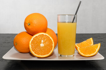 Fresh ripe oranges and glass of juice in a light ceramic dish on dark table. 