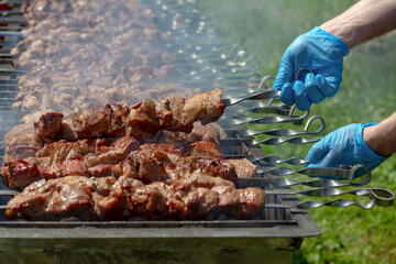 Barbecue, outdoor cooking, barbeque. Skewers of meat on a hot grill closeup. Grilled meat on skewers. Outdoors. On the street. Men's hands in blue gloves, turning skewers with grilled meat.