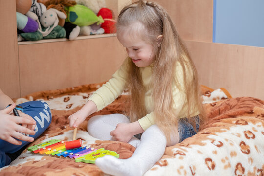 Harmonious Development Of A Child With Down Syndrome. Music Therapy For Children With Down Syndrome. A Girl With Down Syndrome Plays The Scylophone In Her Home.