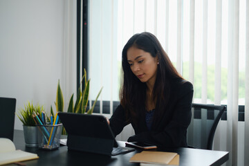 Portrait of beautiful accountant sitting at desk with interior drinking hot beverage holding cup with coffee looking at digital tablet while video conference.