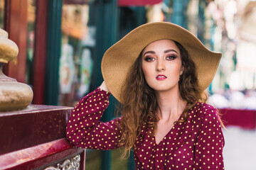 Portrait of a stylish woman in a hat and polka dot dress. Beauty. Polka dot dress. Burgundy in polka dots. Background of vintage shops.