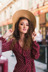 Portrait of a stylish woman in a hat and polka dot dress. Beauty. Polka dot dress. Burgundy in polka dots. Background of vintage shops.