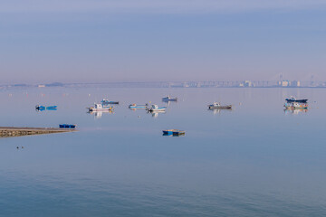 Small fishing boats anchored in harbor near boat ramp on hazy overcast morning.