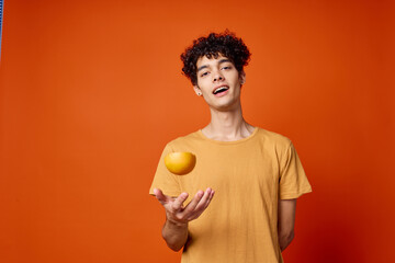 Cheerful curly guy in a yellow t-shirt oranges in his hands red background