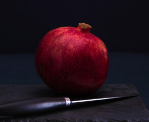 Whole pomegranate fruit on a on a black stone background. A large red pomegranate with a knife next...