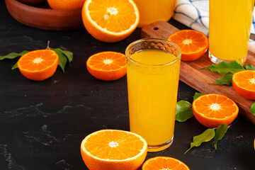 Glass of orange juice and cut oranges on table