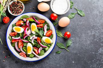 Salad with spinach leaves and eggs in bowl on a dark slate or concrete background. Top view. Copy space.