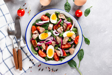 Salad from the liver of codfish, eggs, spinach and tomato on a plate on a light slate, stone or concrete background. Top view. Copy space.