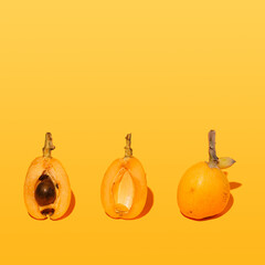 .Unique arrangement three pieces of medlar fruit. A concept made with bright orange background..