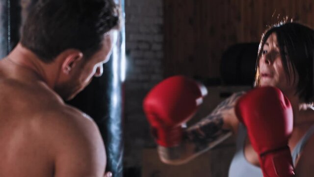 Boxing training in the gym - obstinate woman boxer training her punches on punching bag with trainer