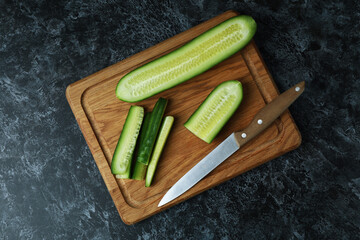 Board with ripe cucumber and knife on black smokey table