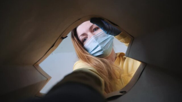 Delivery of groceries to door. Online shopping. Girl in safety mask opens bag of groceries. Safe delivery of groceries. Online Store. Delivery in safety mask to door. Online shopping and delivery