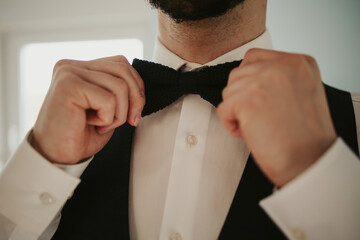 Bearded groom fixing his bow tie and getting prepared for his wedding