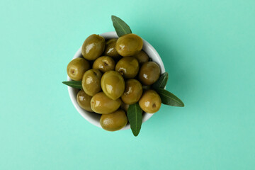 Bowl of green olives and leaves on mint background